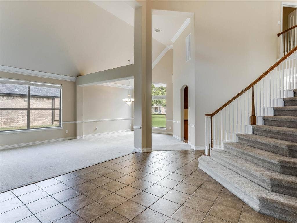 Vaulted ceilings with crown molding, ceramic tile flooring, staircase featuring a wood handrail with white balusters, and large windows