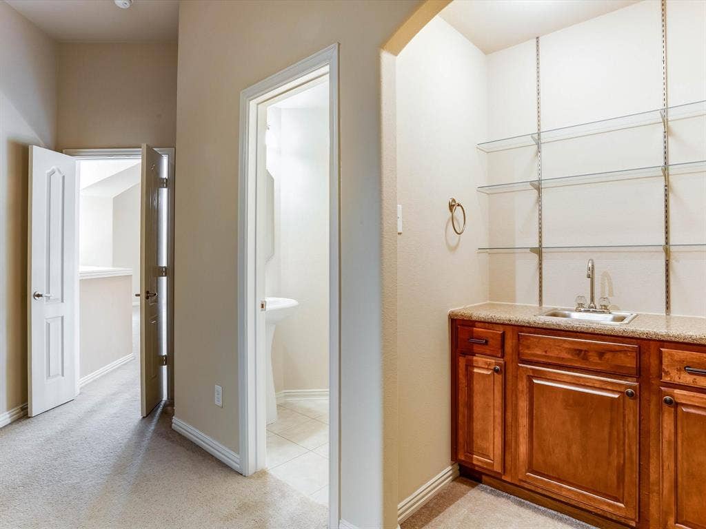 Built-in wet bar featuring stained wood cabinetry, stone-finish countertop, stainless steel sink, and adjustable glass shelving