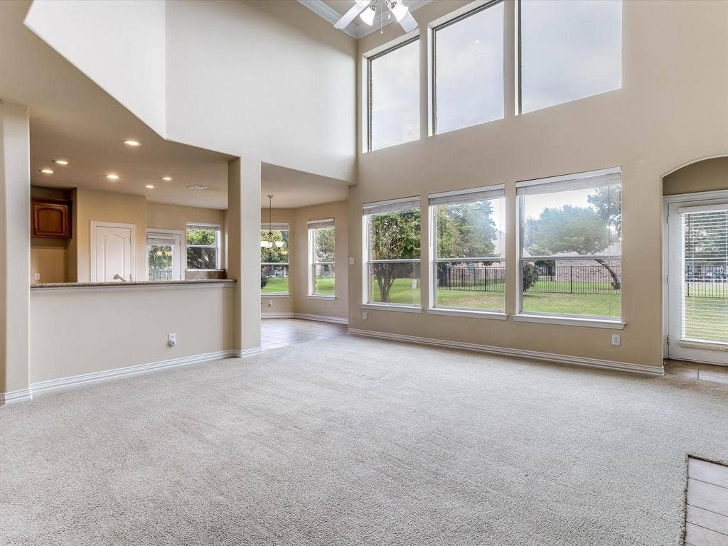 Double-height ceilings, expansive window wall, neutral carpeting, recessed lighting, and a kitchen pass-through counter
