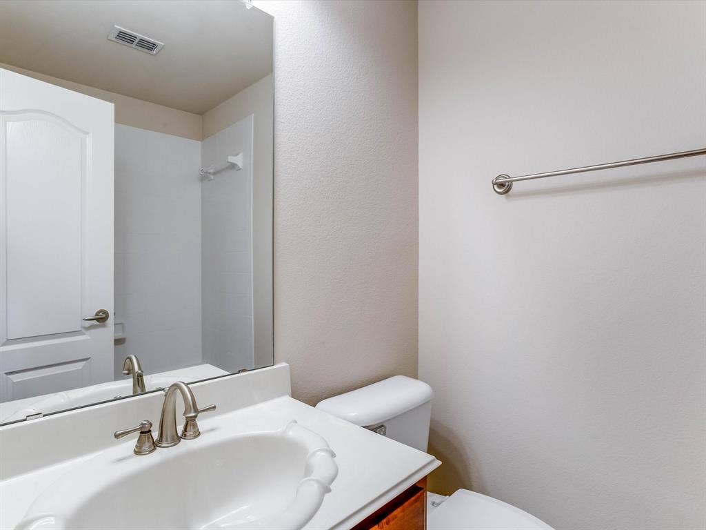 Bathroom featuring a vanity with a white integrated sink and countertop, polished chrome widespread faucet, expansive wall-mounted mirror, and a matching metal towel bar