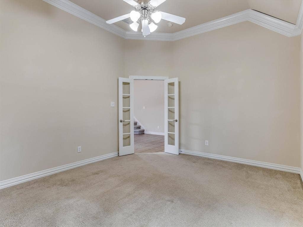 Vaulted ceilings featuring decorative crown molding, white French doors, and a central ceiling fan with multi-light fixture