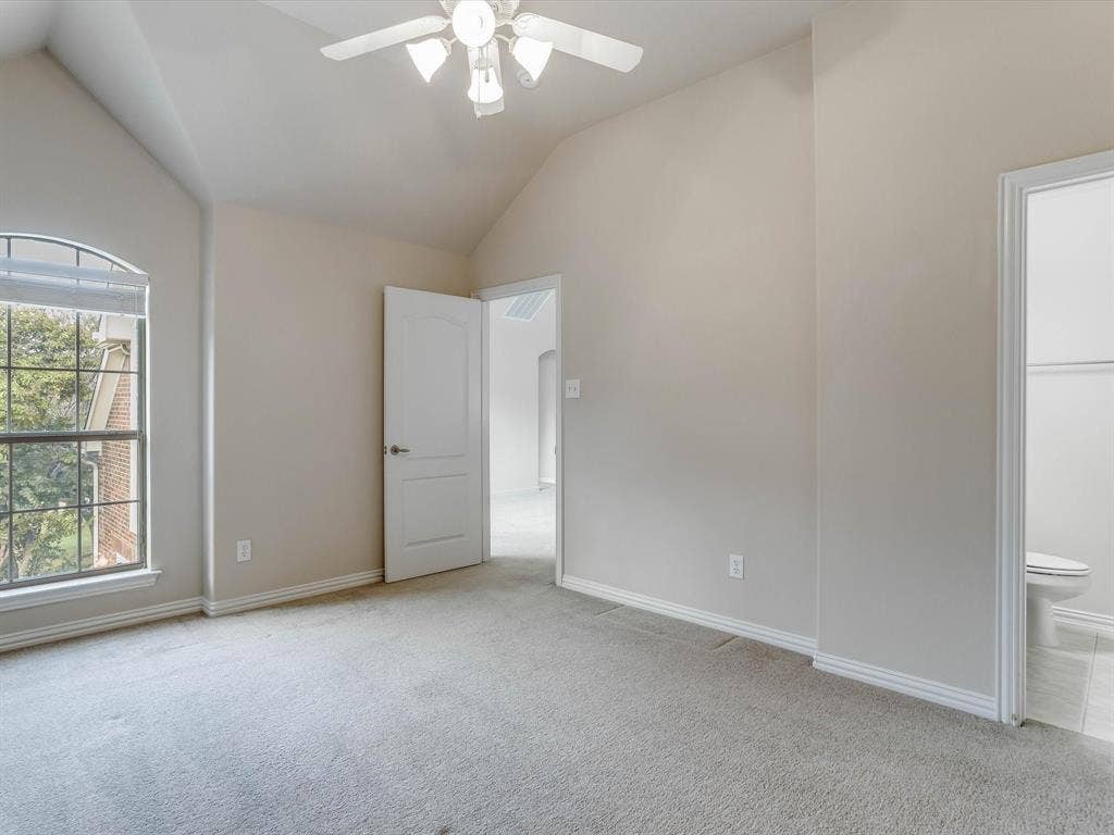 Vaulted ceilings, arched window with grid detail, neutral wall tones, carpeted flooring, and ceiling fan with integrated lighting
