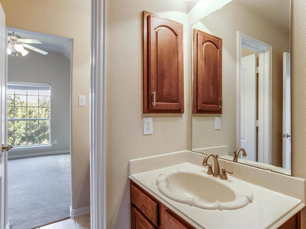 Bathroom featuring a vanity with wood-finish cabinetry, an integrated sink basin, a decorative high-back mirror, and brass-tone hardware