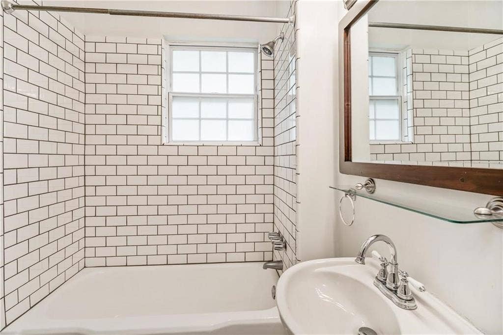 5936 Bryan Parkway, #B, Dallas, TX 75206 Bathroom featuring white subway tile surround, integrated bathtub, grid-pattern window, pedestal sink with chrome faucet, and wood-framed mirror