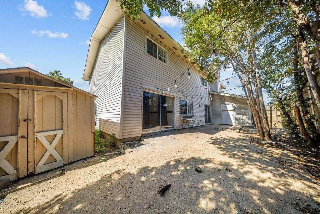 738 Intrepid Drive, Garland, TX 75043 Exterior rear elevation featuring light-toned vinyl siding, a concrete patio, and a detached wooden storage shed