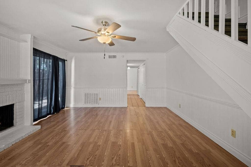 738 Intrepid Drive, Garland, TX 75043 Living area featuring wood-finish flooring, a painted brick fireplace, beadboard wainscoting, a ceiling fan with integrated lighting, and a staircase with white balusters
