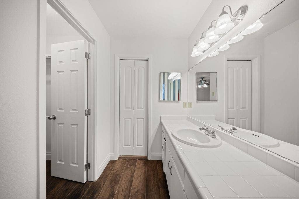 738 Intrepid Drive, Garland, TX 75043 Vanity featuring a tile countertop, integrated oval basin, white cabinetry, wood-finish flooring, and a full-width wall mirror