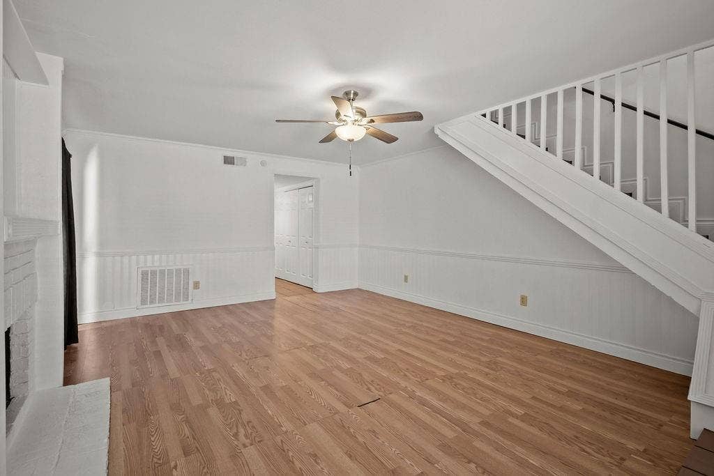 738 Intrepid Drive, Garland, TX 75043 Interior space featuring wood-finish flooring, wainscoting, a fireplace with a painted brick surround, a ceiling fan with integrated lighting, and a staircase with white balusters