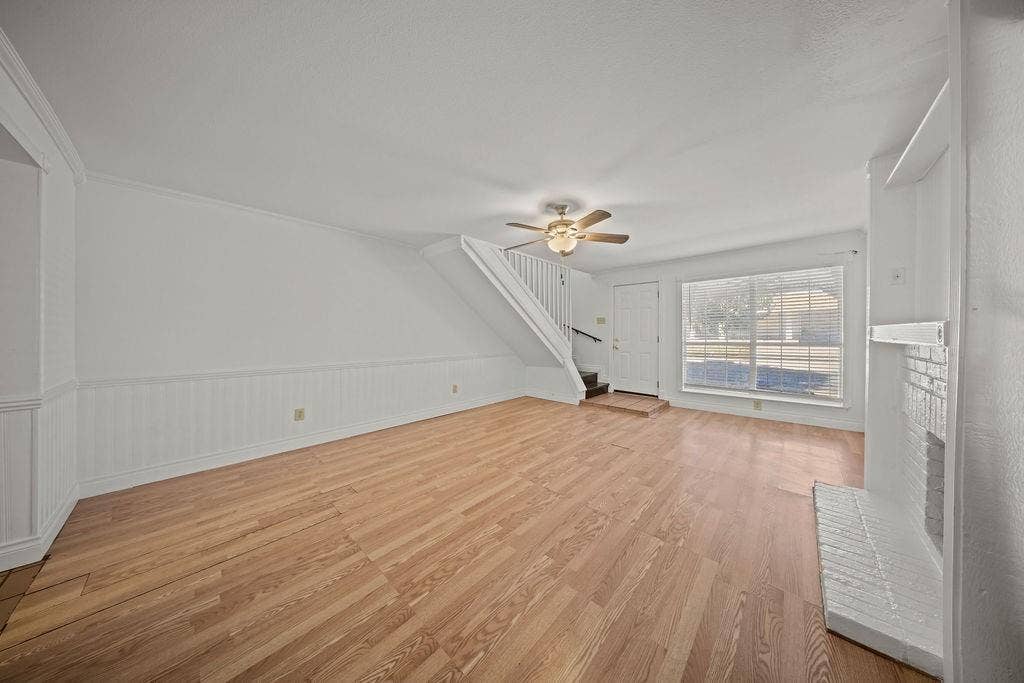 738 Intrepid Drive, Garland, TX 75043 Living space featuring wood-finish flooring, white wainscoting, a painted brick fireplace, and a ceiling fan