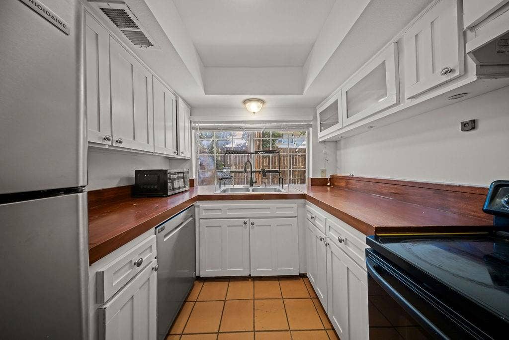 738 Intrepid Drive, Garland, TX 75043 Kitchen featuring white shaker-style cabinetry with glass-front uppers, wood-finish countertops, stainless steel appliances, a double-basin sink with a matte black pull-down faucet, and ceramic tile flooring