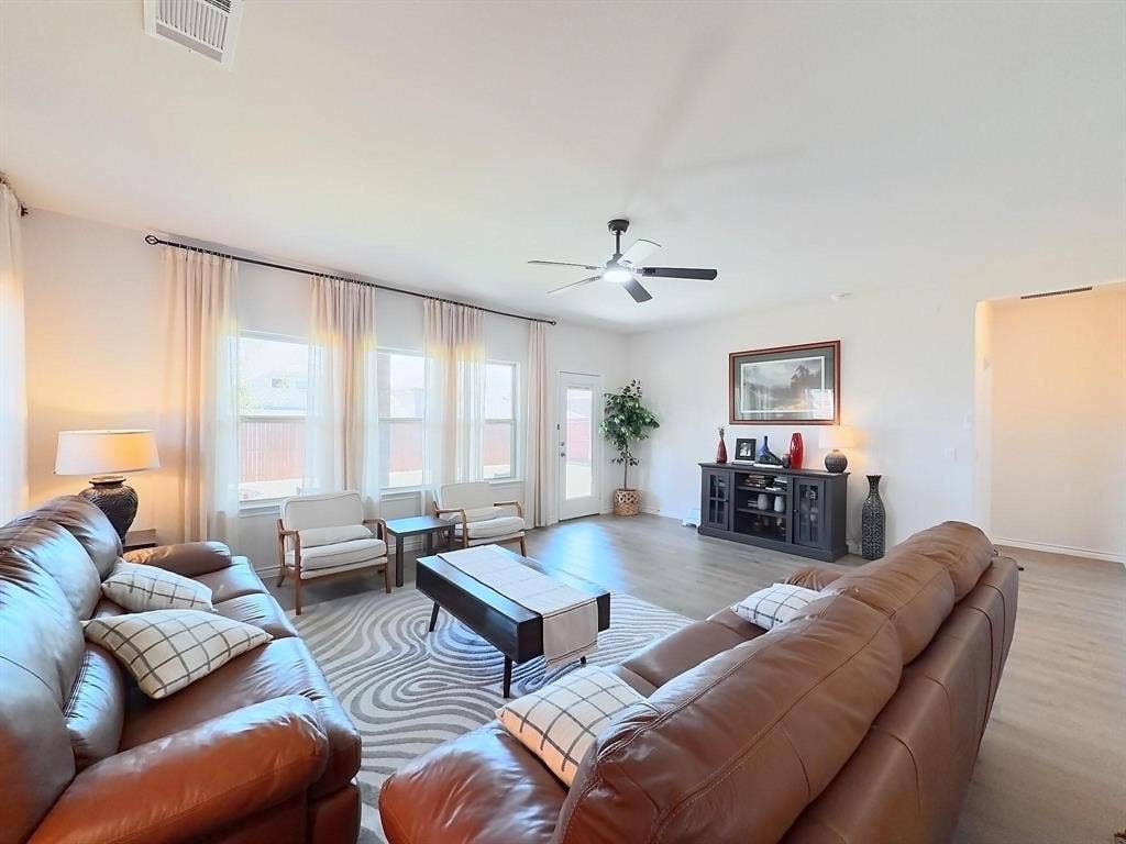 7400 Seton Place, McKinney, TX 75071 Open-concept living space featuring wood-finish flooring, high ceilings, a ceiling fan, and large windows with curtain hardware