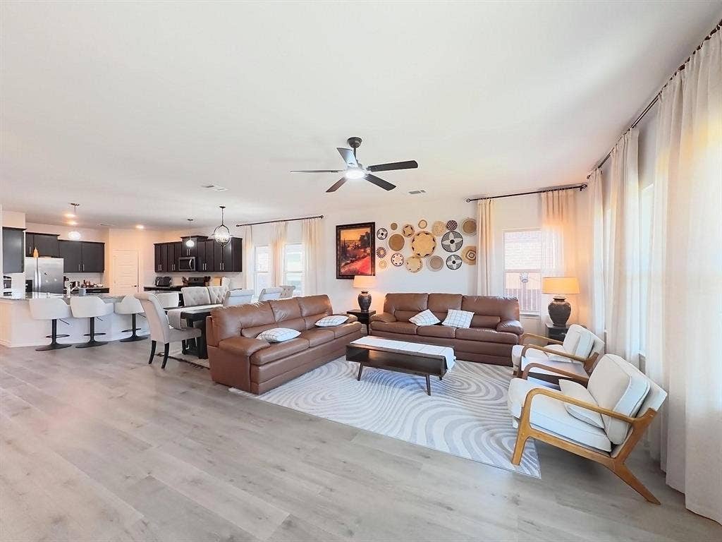 7400 Seton Place, McKinney, TX 75071 Open-concept interior featuring light-toned wood-finish flooring, a kitchen island with stone-surface countertop, dark-finish cabinetry, and a ceiling fan with integrated lighting