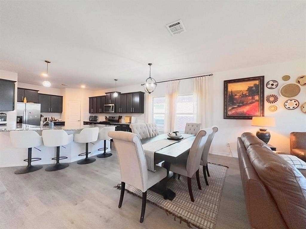 7400 Seton Place, McKinney, TX 75071 Open concept kitchen featuring dark cabinetry, stone-finish countertops, stainless steel appliances, and a breakfast bar with three pendant lights