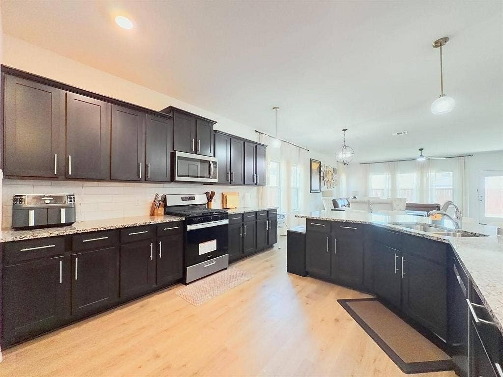 7400 Seton Place, McKinney, TX 75071 Kitchen featuring dark cabinetry, speckled stone-finish countertops, wood-finish flooring, a white tile backsplash, and stainless steel appliances
