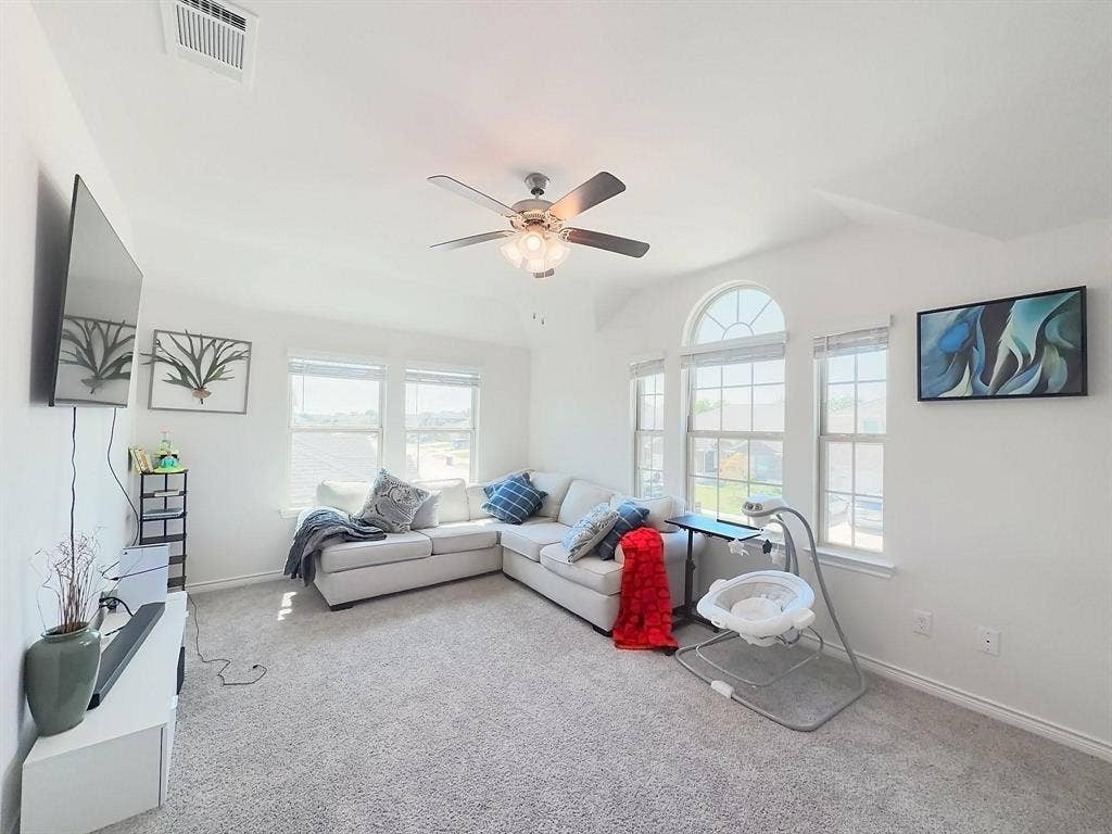 7400 Seton Place, McKinney, TX 75071 Living area featuring neutral carpeting, a vaulted ceiling, a multi-blade ceiling fan with integrated lighting, and multiple windows including an arched window element