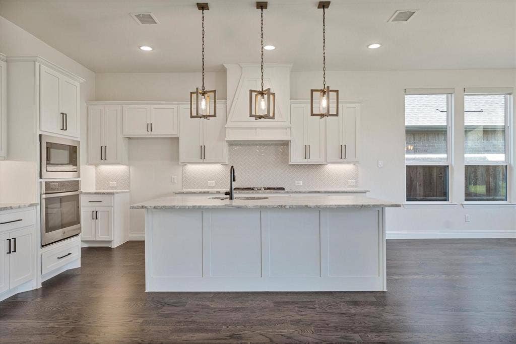 2817 Yarmouth Street, Celina, TX 75009 Kitchen featuring white cabinetry, center island with stone countertop, herringbone tile backsplash, stainless steel double wall ovens, and three geometric pendant lights over the island