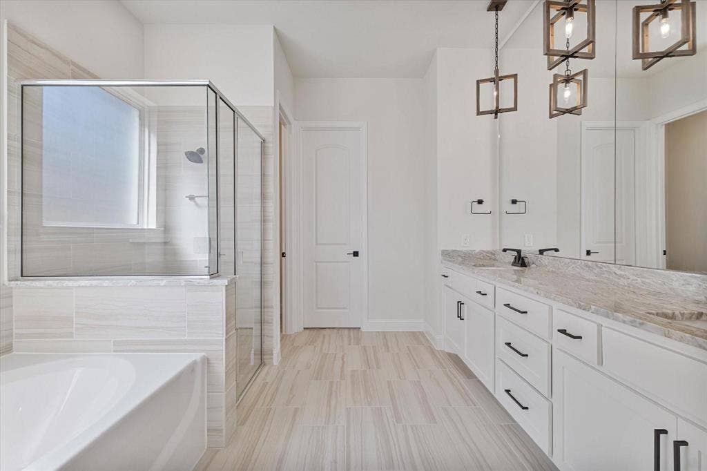 2817 Yarmouth Street, Celina, TX 75009 Dual-sink vanity with stone-finish countertops and matte black hardware, tiled walk-in shower with glass enclosure, freestanding soaking tub, and geometric pendant lighting