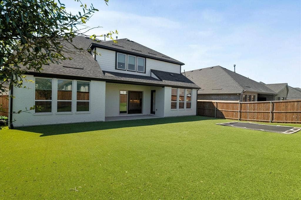 2817 Yarmouth Street, Celina, TX 75009 Rear exterior featuring a white brick and horizontal siding facade, multiple large windows, a paved patio, and a fully fenced private yard