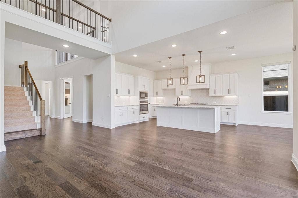 2817 Yarmouth Street, Celina, TX 75009 Open-concept interior featuring wood-finish flooring, a double-height ceiling, a center island with pendant lighting, white shaker-style cabinetry, and a carpeted staircase with a wood railing