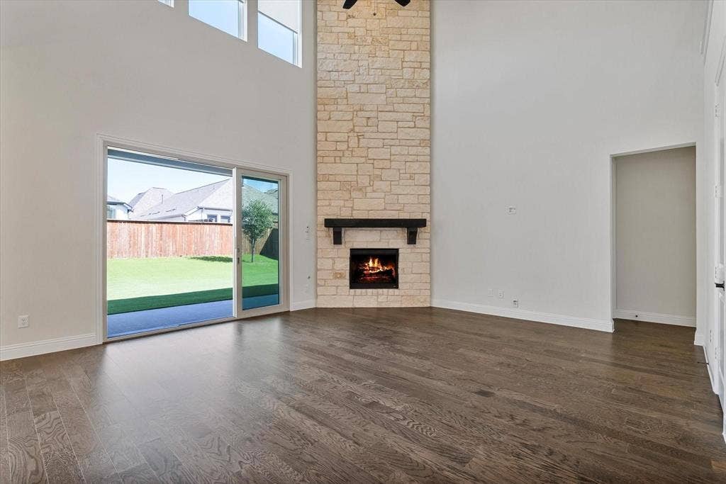 2817 Yarmouth Street, Celina, TX 75009 Double-height living area featuring wood-finish flooring, floor-to-ceiling stone fireplace, dark wood mantel, and sliding glass doors