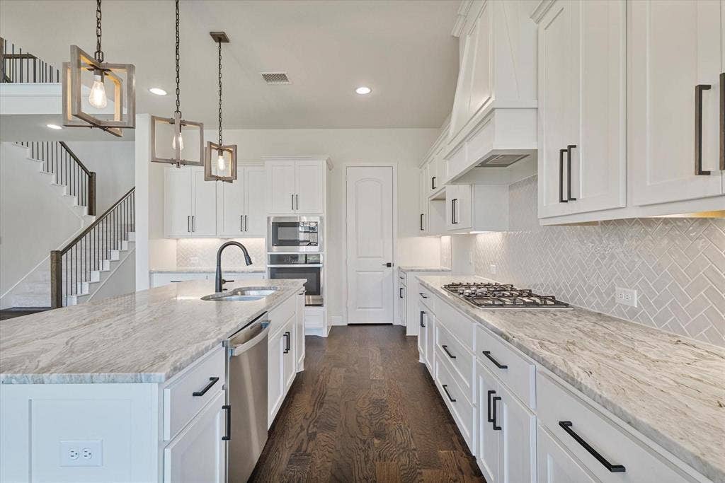 2817 Yarmouth Street, Celina, TX 75009 Kitchen featuring white shaker-style cabinetry, patterned stone countertops, a herringbone tile backsplash, stainless steel built-in appliances, and wood-finish flooring