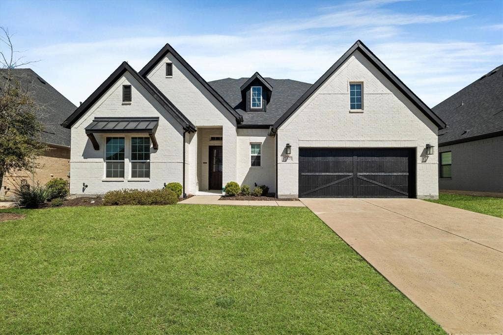 2817 Yarmouth Street, Celina, TX 75009 Light-colored brick exterior featuring a multi-gabled roofline, dark-toned carriage-style garage door, metal awning detail, and recessed entry
