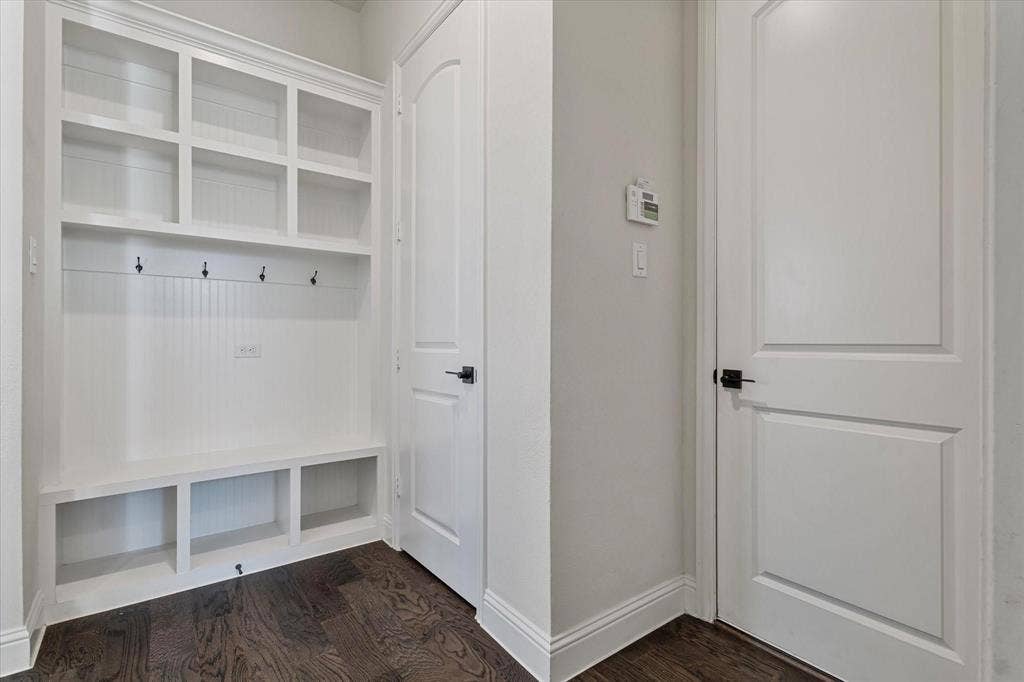 2817 Yarmouth Street, Celina, TX 75009 Built-in white storage cabinetry with beadboard paneling, integrated coat hooks, open shelving, and wood-finish flooring accented by arched-panel interior doors with matte black hardware