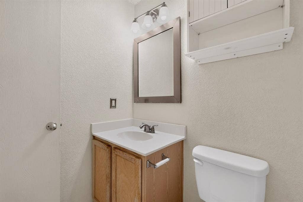 3107 Westview Drive, McKinney, TX 75070 Vanity cabinet with integrated solid-surface countertop and undermount sink, brushed-nickel hardware, framed wall mirror, three-light vanity fixture, and white wall-mounted cabinetry