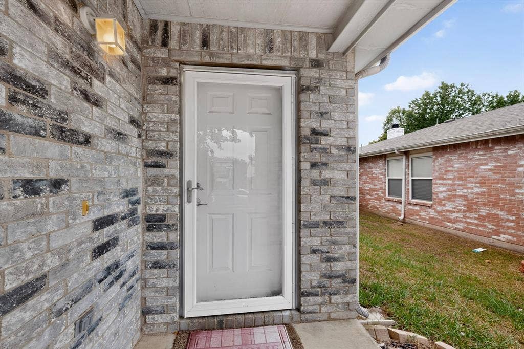 3107 Westview Drive, McKinney, TX 75070 Entryway featuring multi-toned grey brick facade, white storm door, and mounted exterior lighting fixture