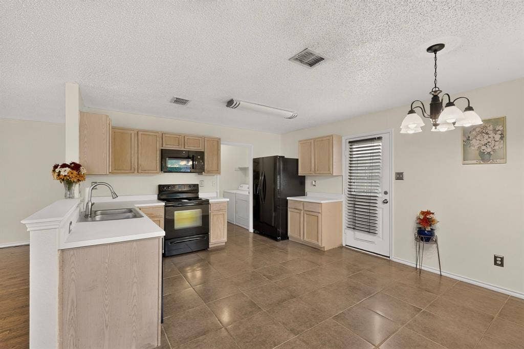 3107 Westview Drive, McKinney, TX 75070 Kitchen featuring light-finish cabinetry, neutral-toned tile flooring, integrated black appliances, and a traditional multi-light chandelier