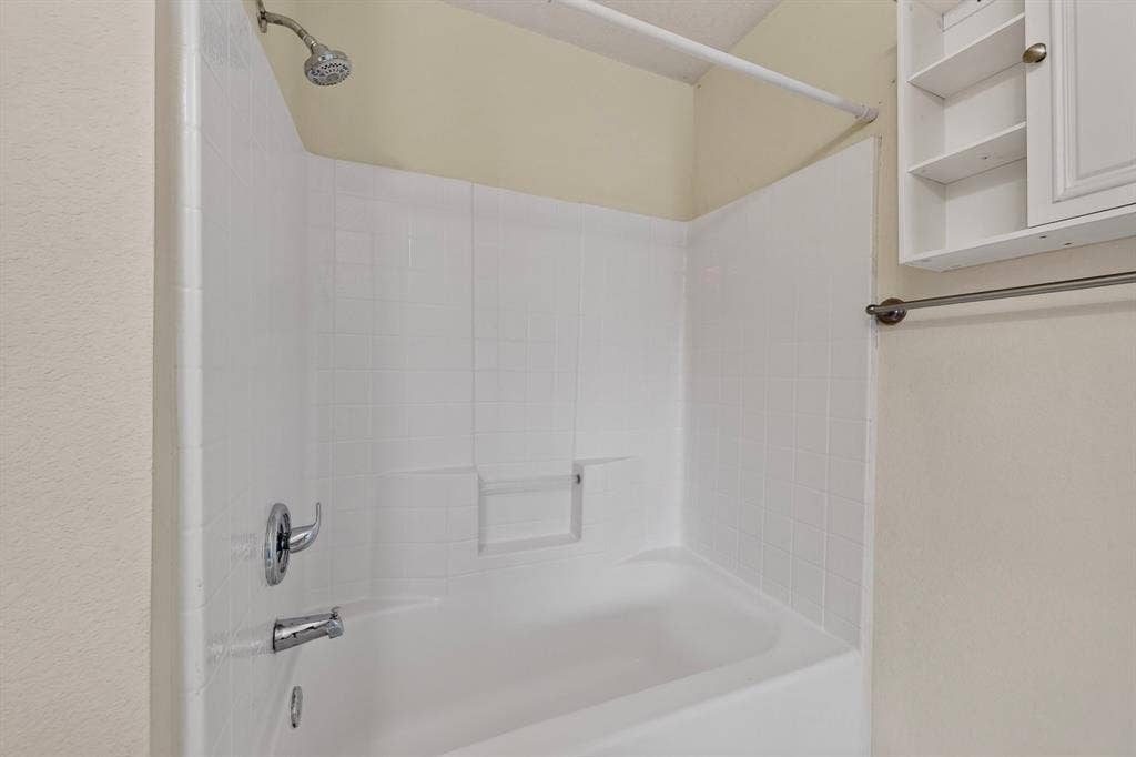 3107 Westview Drive, McKinney, TX 75070 Bathtub featuring a white tiled surround with integrated shelving, chrome-finish fixtures, and built-in wall-mounted cabinetry