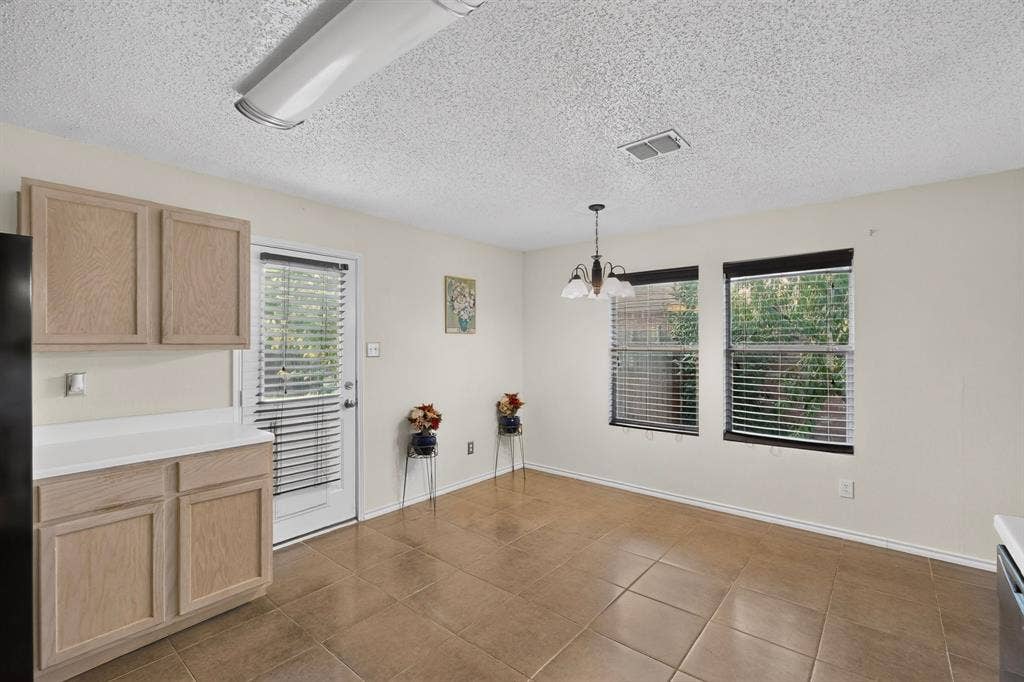 3107 Westview Drive, McKinney, TX 75070 Neutral-toned tile flooring, light wood-finish cabinetry, solid surface countertops, a multipane glass-panel exterior door, and hanging pendant lighting