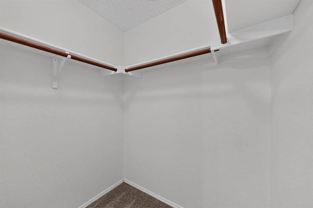3107 Westview Drive, McKinney, TX 75070 Walk-in closet featuring white wall-mounted shelving with dual wooden hanging rods and wall-to-wall carpeting