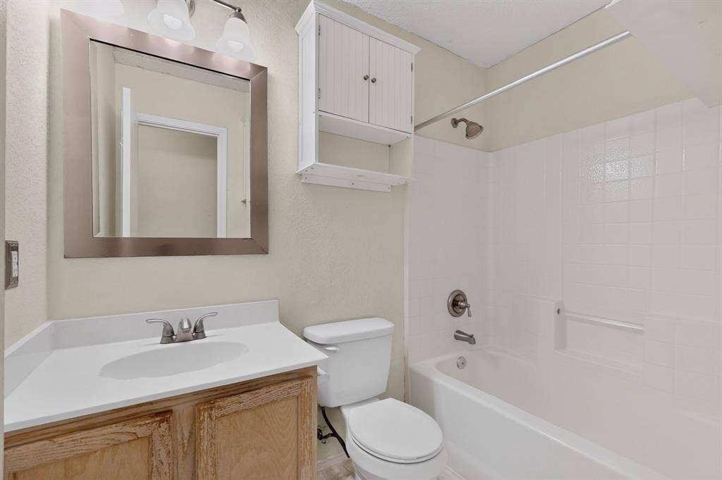 3107 Westview Drive, McKinney, TX 75070 Bathroom featuring a vanity with a white solid-surface countertop, an integrated sink, a wall-mounted wooden cabinet, and a tiled tub-and-shower combination