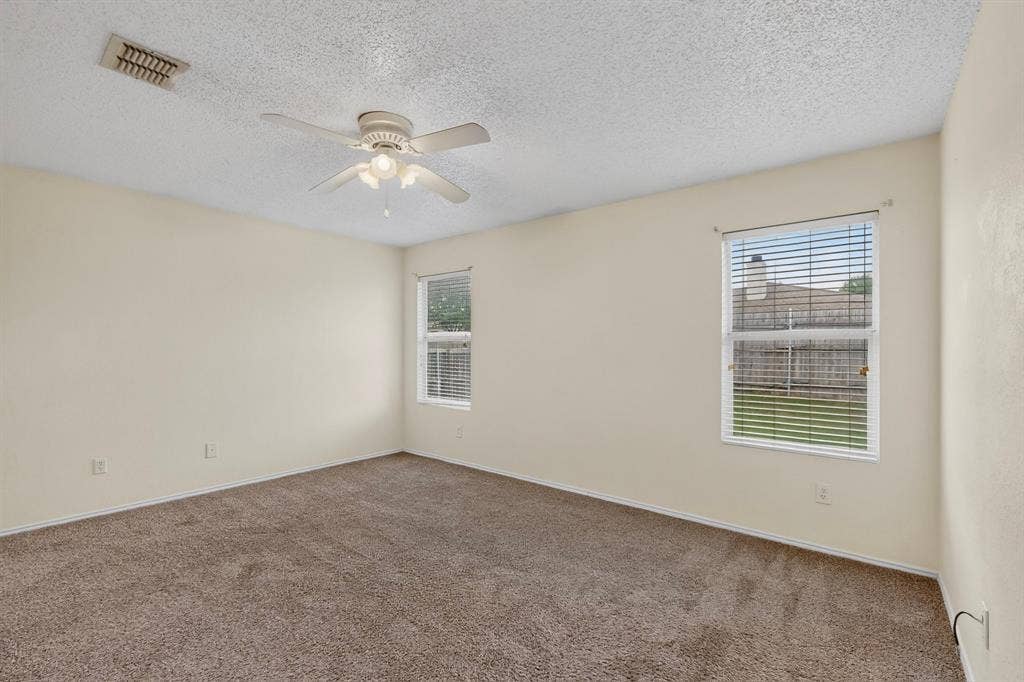 3107 Westview Drive, McKinney, TX 75070 Neutral-toned interior space featuring carpeted flooring, two windows with horizontal blinds, and a ceiling-mounted light fixture with a fan