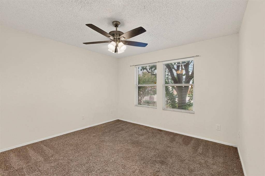 3107 Westview Drive, McKinney, TX 75070 Neutral-toned interior space featuring textured ceiling, carpeting, multi-blade ceiling fan with integrated lighting, and dual windows with metal rods