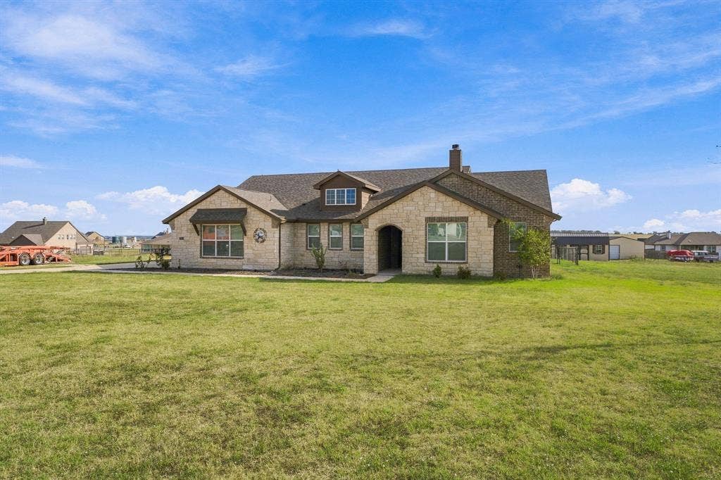 Single-story exterior featuring a natural stone facade, dark composition shingle roof, arched entryway, and multiple gabled rooflines