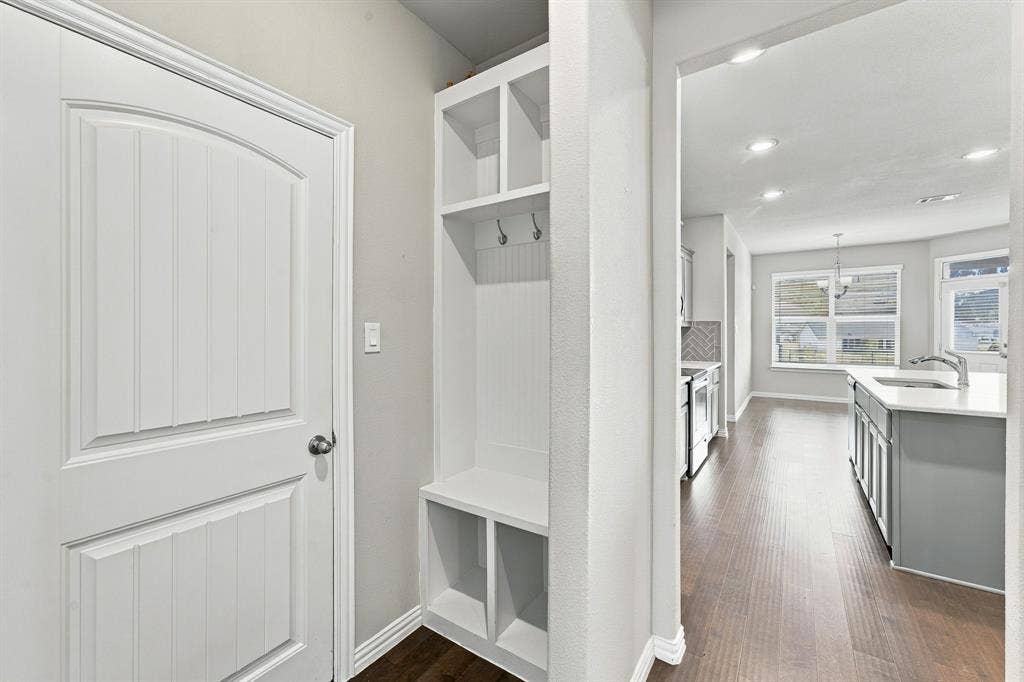 Built-in entryway hall tree with bench seating, custom beadboard backing, and metal hooks, featuring wood-finish flooring and a multi-panel door