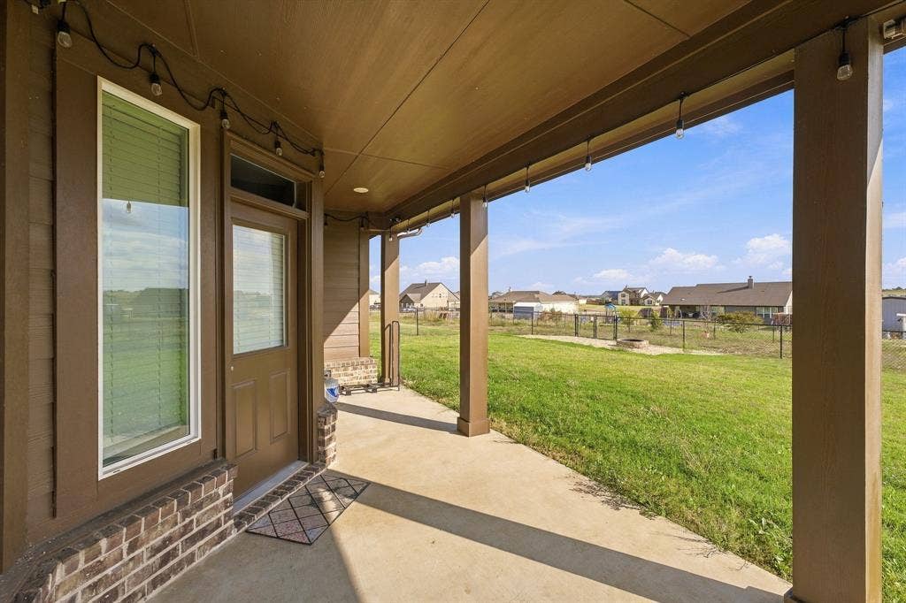 Covered patio featuring concrete flooring, structural support columns, brick masonry base, and a door with an integrated transom window
