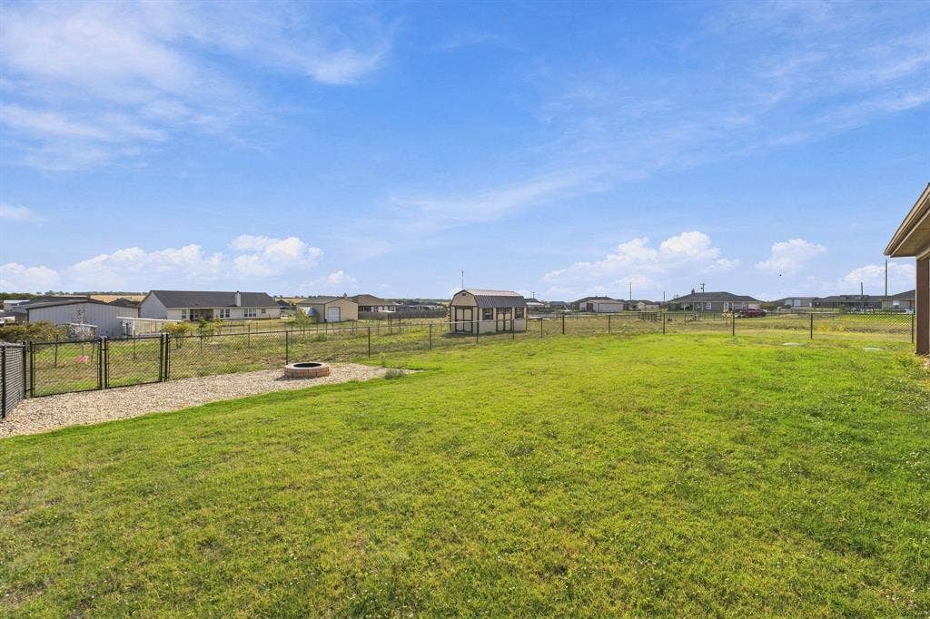Expansive backyard featuring a fenced perimeter, stone-bordered fire pit, and detached storage structure