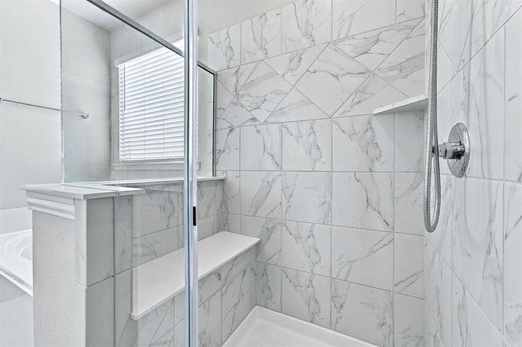 Walk-in shower featuring floor-to-ceiling stone-pattern tile, a built-in bench, a glass enclosure, and a chrome adjustable-height shower head