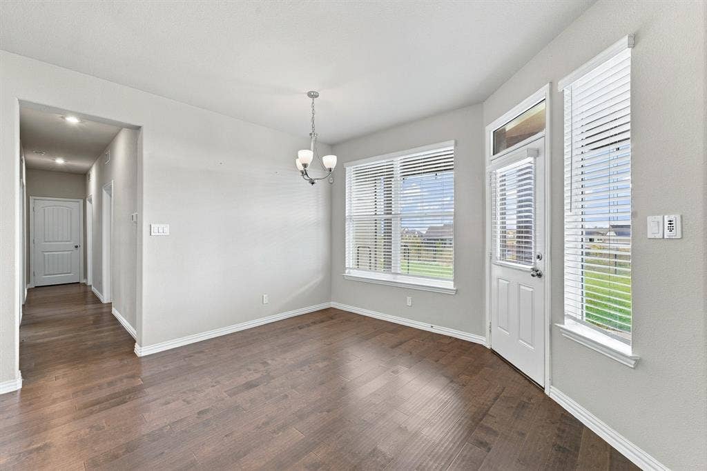 Interior space featuring dark wood-finish flooring, multi-pane windows with integrated blinds, a single-light exterior door with a transom window, and a three-bulb chandelier