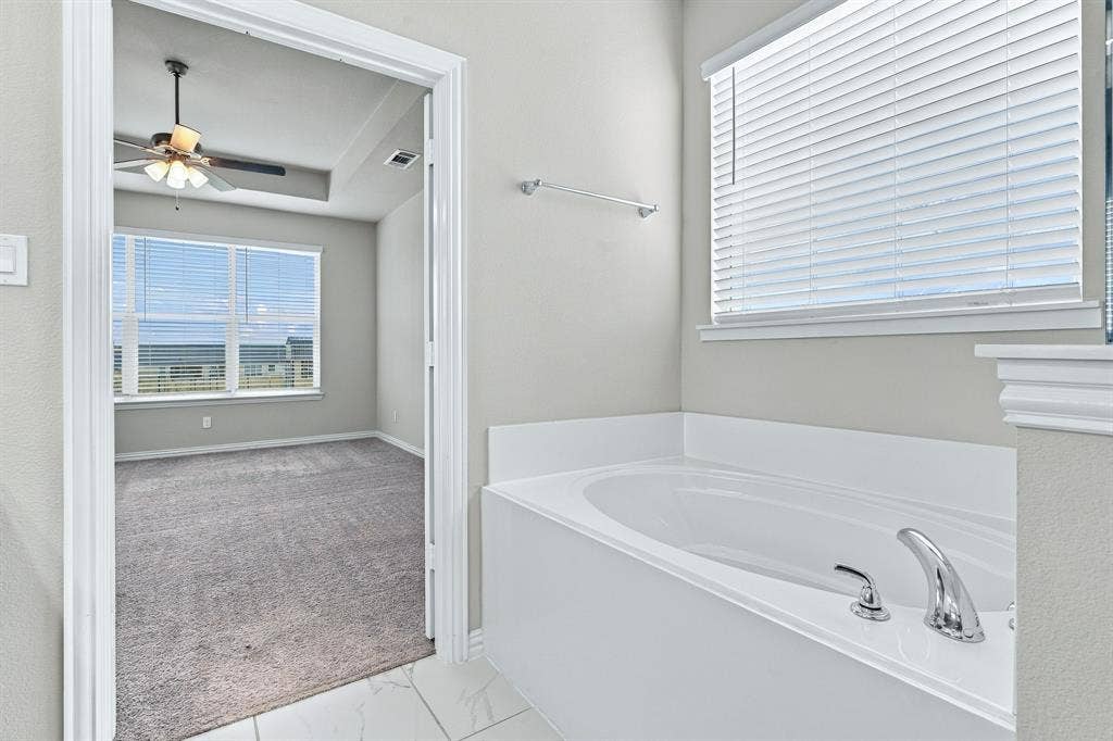Built-in soaking tub with chrome faucet hardware, tile flooring, window blinds, and overhead ceiling fan