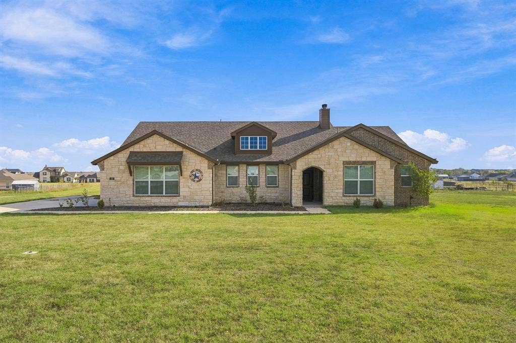 Stone veneer facade, multi-gabled roofline, dormer window, covered arched entryway, and expansive front lawn