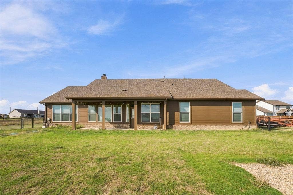 Rear exterior featuring horizontal lap siding, a brick water table, an expansive grassy yard, and a covered patio with support columns