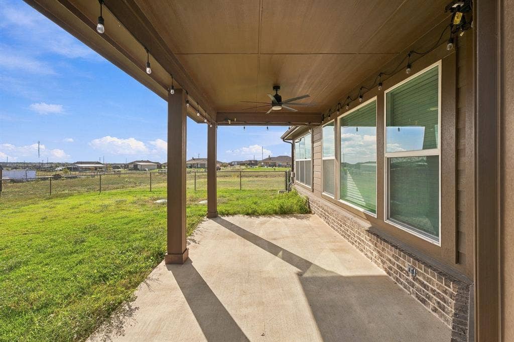 Covered concrete patio featuring a ceiling fan and exterior string light fixtures, set against a backdrop of open greenspace