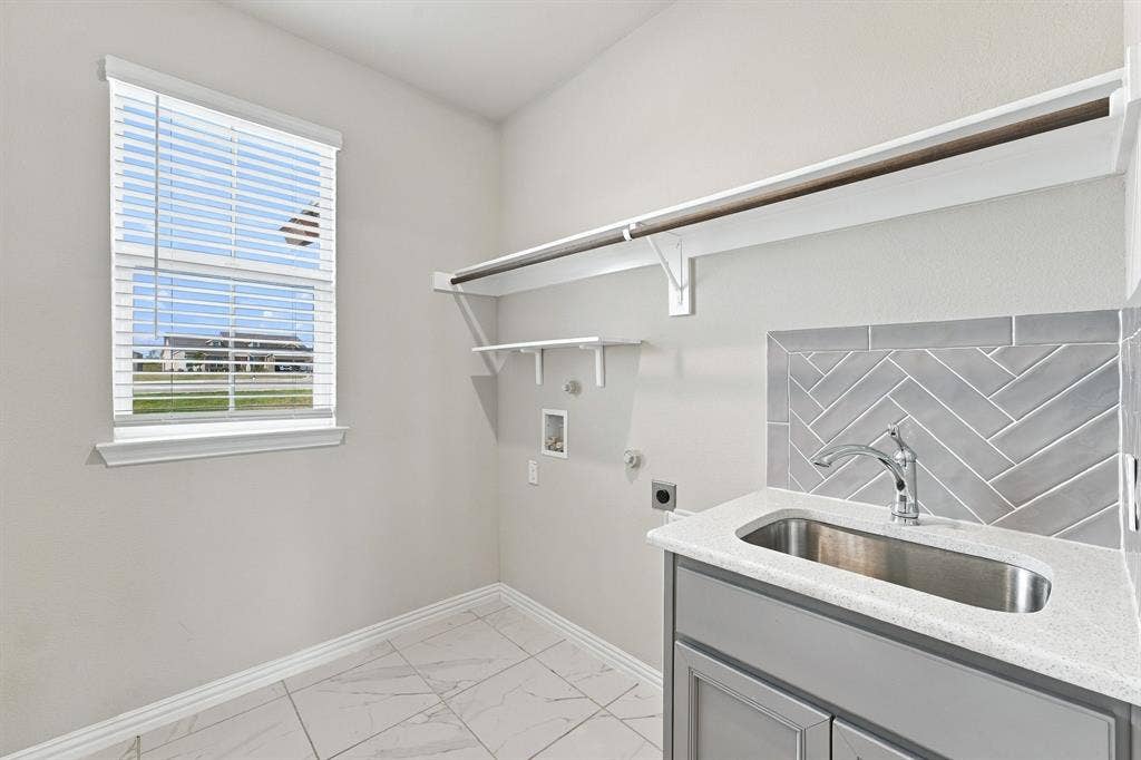 Laundry room featuring a stainless steel drop-in sink, quartz countertop, herringbone tile backsplash, gray cabinetry, and patterned tile flooring