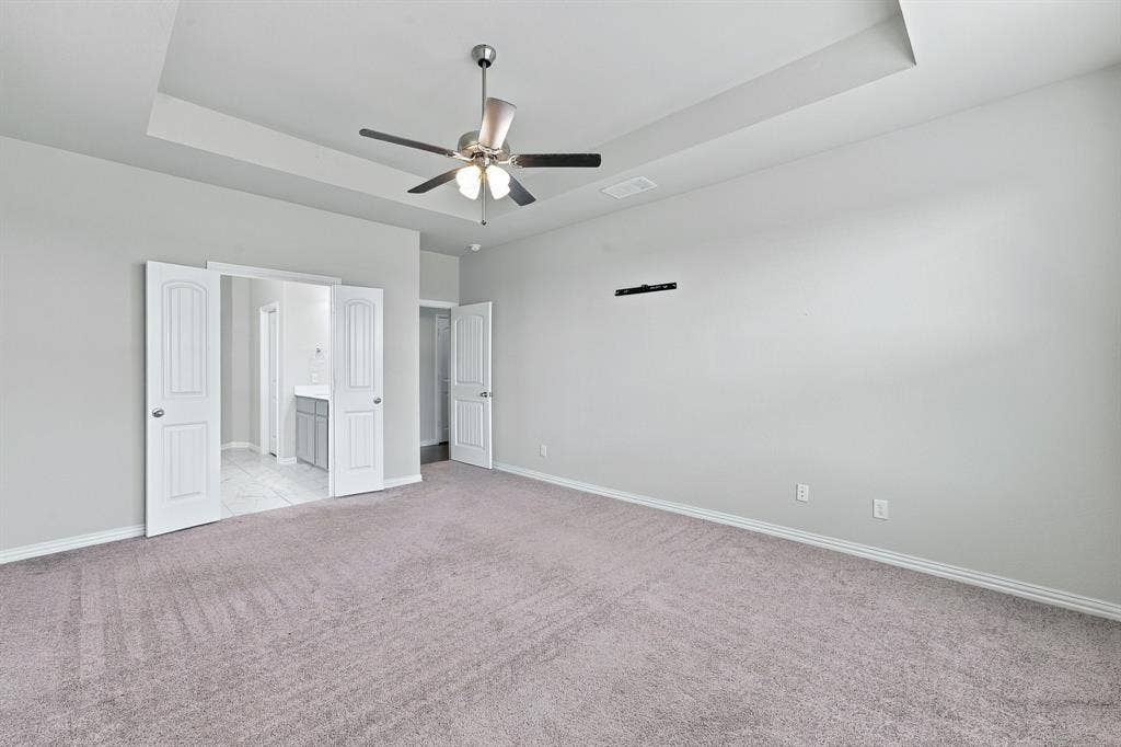 Tray ceiling featuring a central brushed-nickel ceiling fan with integrated lighting, wall-to-wall carpeting, and interior double doors