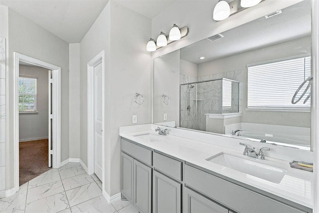 Dual-sink vanity with gray cabinetry and solid-surface countertop, full-width vanity mirror, tile flooring, and walk-in shower with tiled surround