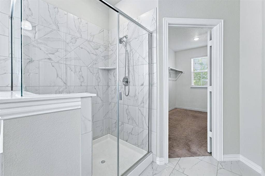 Walk-in shower featuring glass enclosure, large-format tile surround, and handheld showerhead, complemented by matching tile flooring and built-in closet shelving